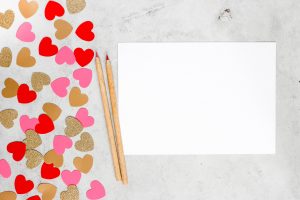 blank piece of paper ready to be decorated with cut-out hearts and red and pink pencils